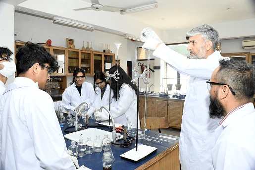 Students in lab coats running a chemistry experiment with their teacher.